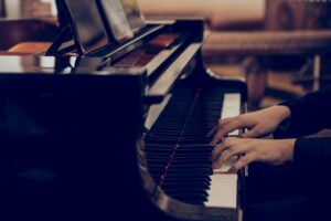 Person playing a grand piano, hands positioned on the keys, with sheet music visible on the stand.